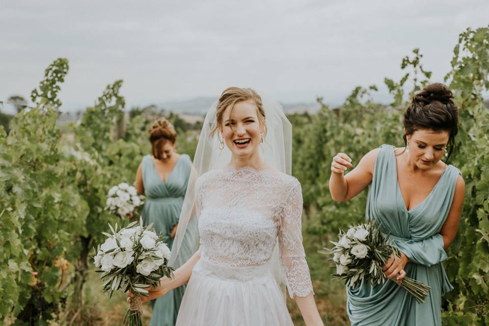 A laughing bride and bridesmaids among rows of grapevines at Oakridge Wines