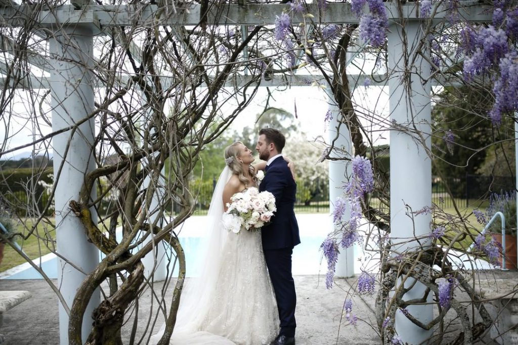 A couple kissing near blooming wisteria at Coombe Yarra Valley