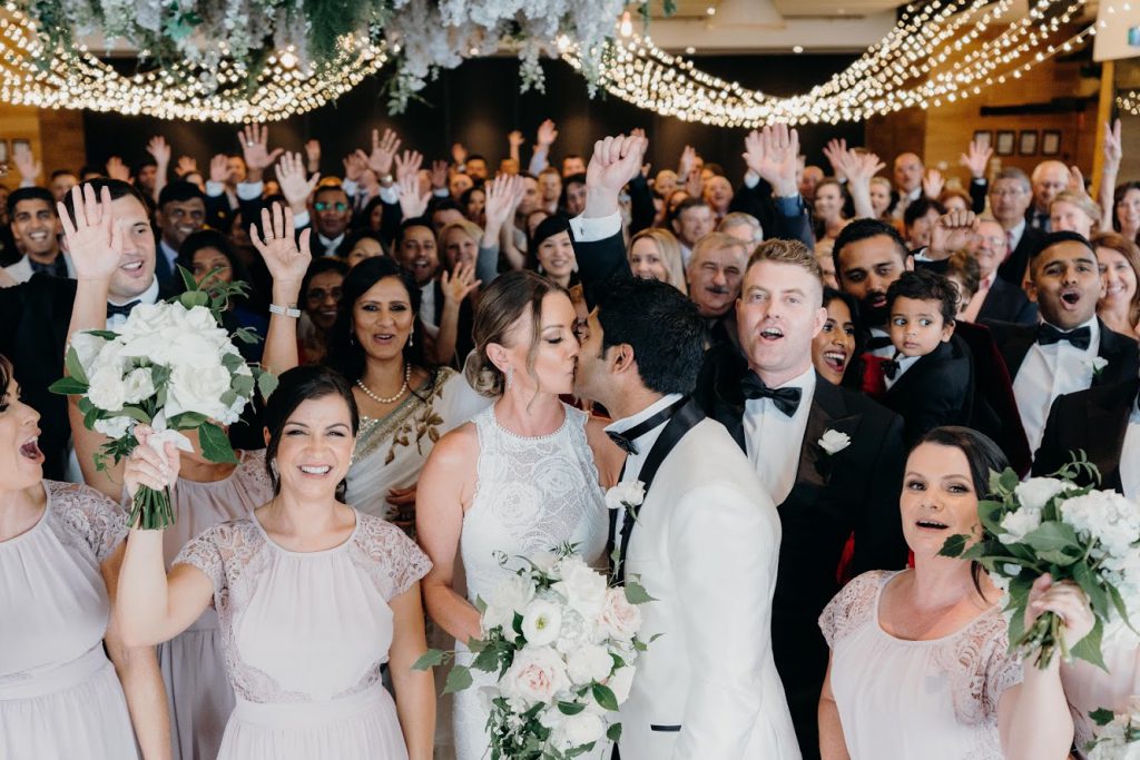 A couple kiss surrounded by wedding guests