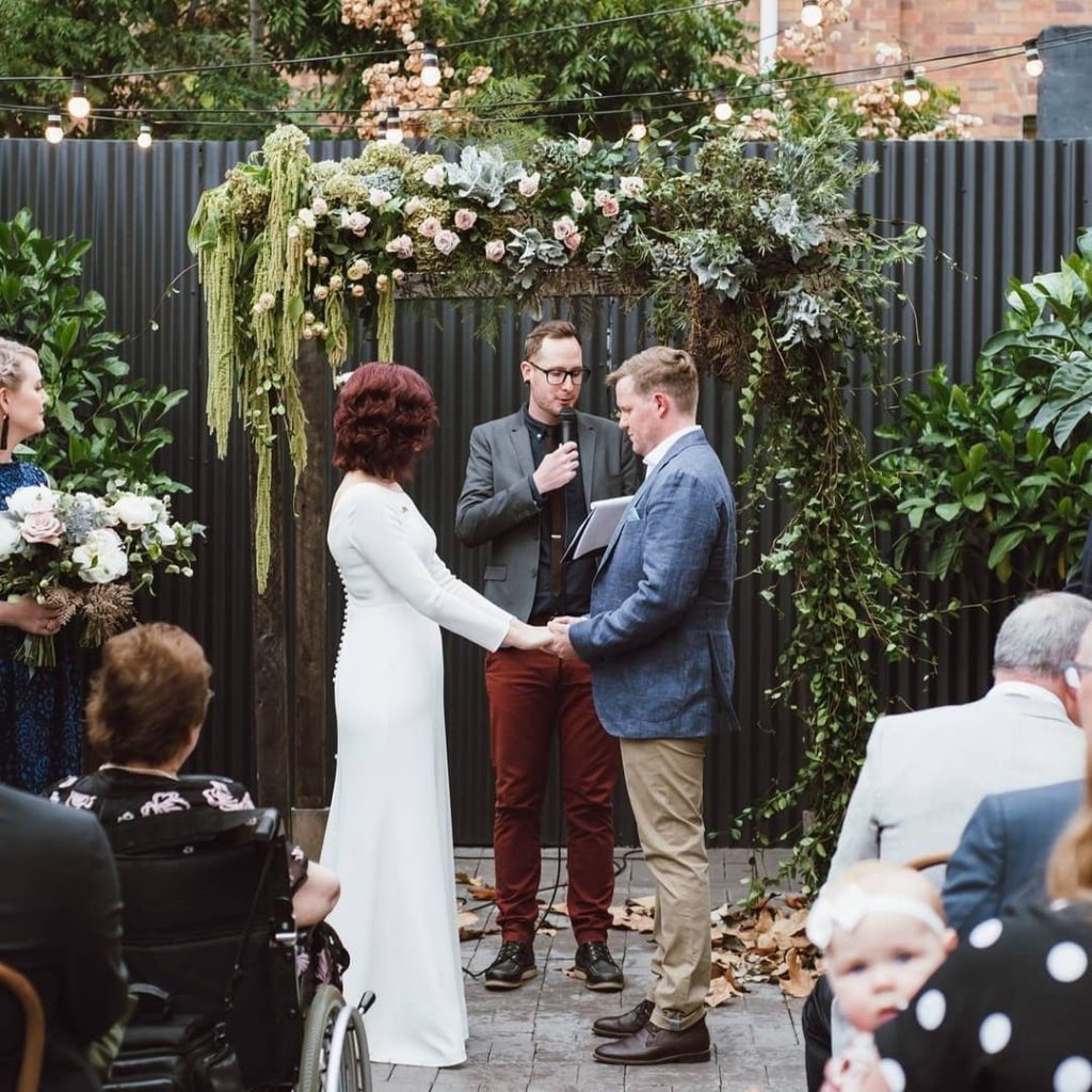 A wedding couple is exchanging the vow , a celebrant and guests