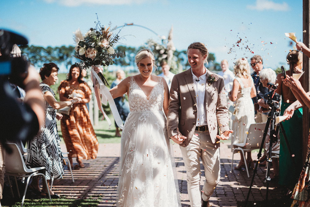 A couple is walking away from the ceremony alley, smiling at Oneday Estate