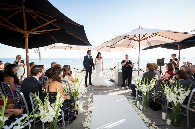 A wedding couple is holding hands with blue ocean as a backdrop