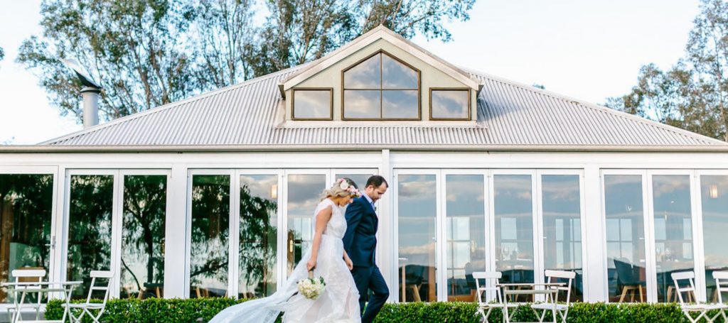 A couple holding hand walking in front of a building with floor to ceiling windows