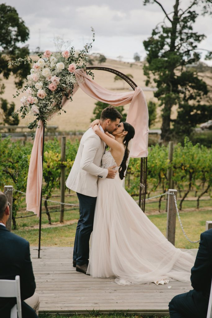 Intimate Winery Wedding Venues Melbourne - The Little Vineyards A couple is kissing with vineyards as the backdrop