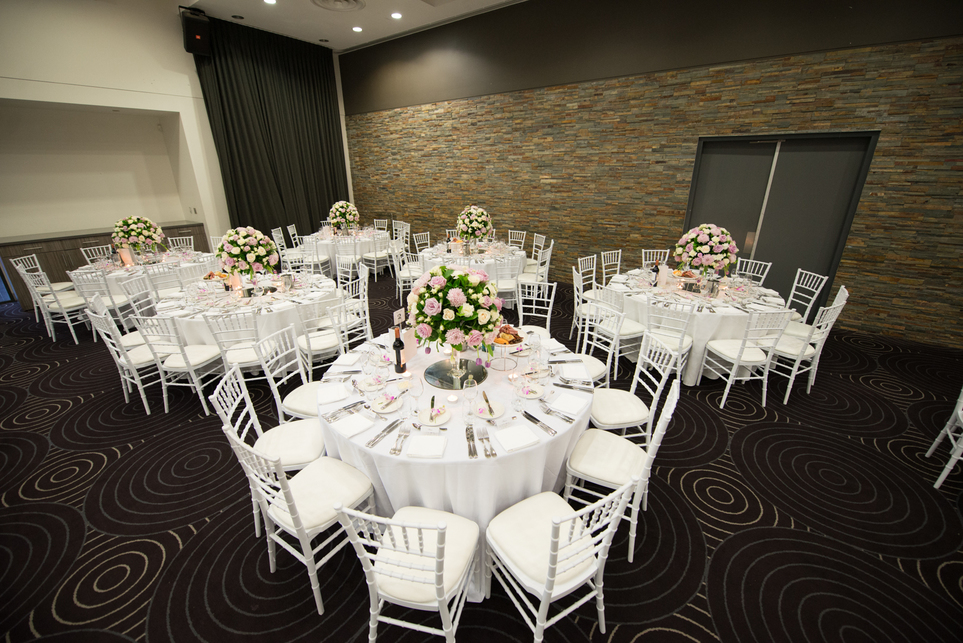 A wedding reception with six round tables on the frame and flowers on each table