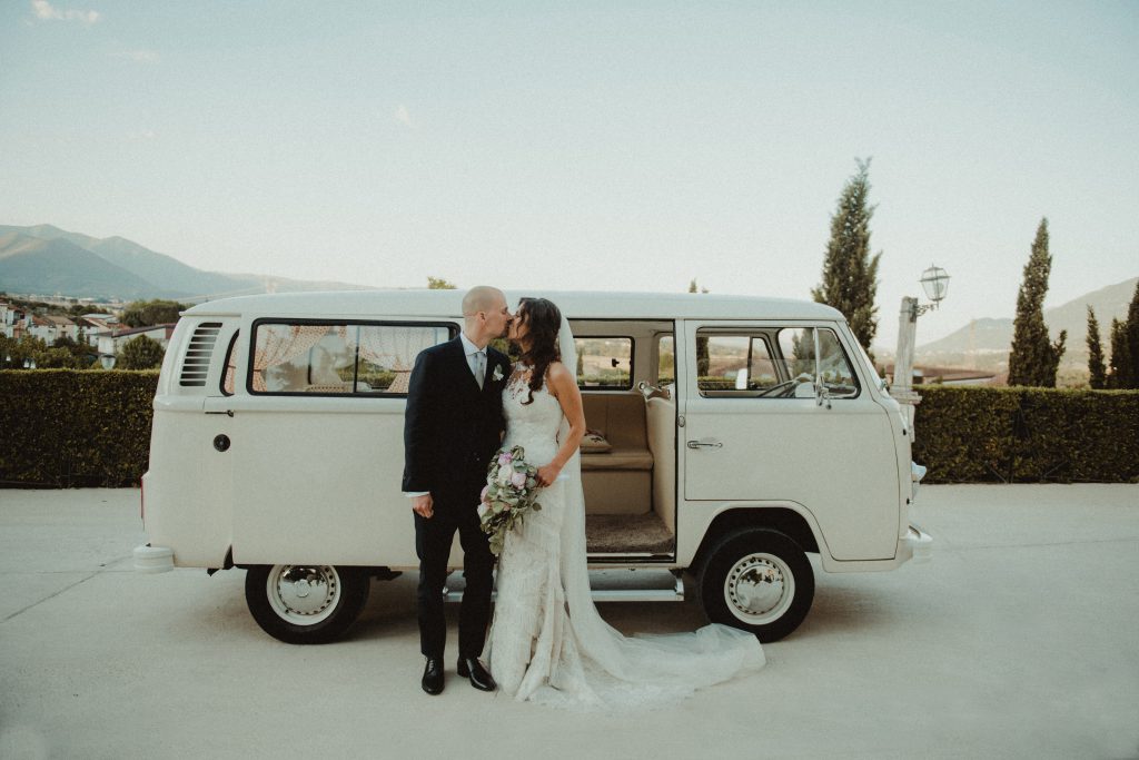 A wedding couple kissing in front of a van